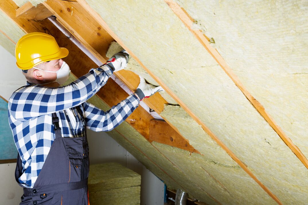 man wearing PPE installing fiberglass insulation in an attic space