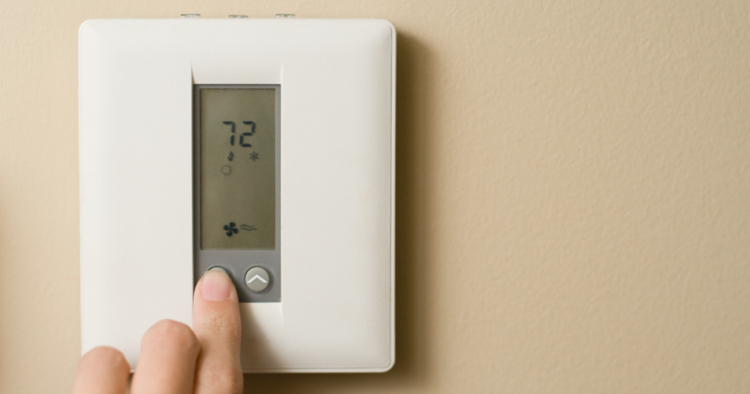 Person turning down temperature on thermostat
